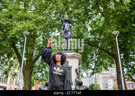 Jen Reid posiert vor ihrer schwarzen Harz- und Stahlstatue mit dem Titel A Surge of Power (jen Reid) 2020 von Marc Quinn, wo sie auf dem leeren Edward Colston Sockel im Stadtzentrum von Bristol installiert wird. Stockfoto