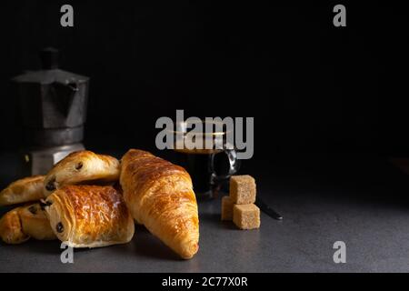 Frühstück mit Croissants, Zimtbrötchen und Schokoladenplätzchen, frischem Orangensaft und Kaffee auf der Seite auf dunklem Hintergrund in einer Lichtquelle. Stockfoto