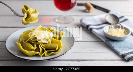 Hausgemachte Bio-Tortellini mit Spinat und Käse auf einem weißen Tisch mit einem Glas Wein auf der Seite. Stockfoto