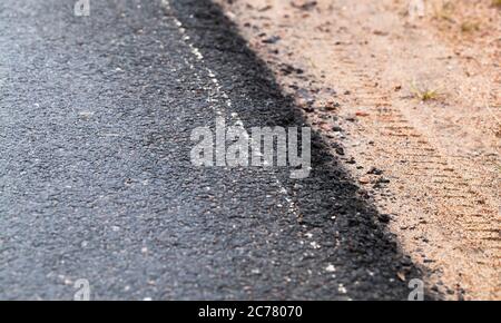 Neue Asphaltstraße und sandige Straßenrand. Abstraktes Transport-Hintergrundbild mit selektivem Weichfokus Stockfoto