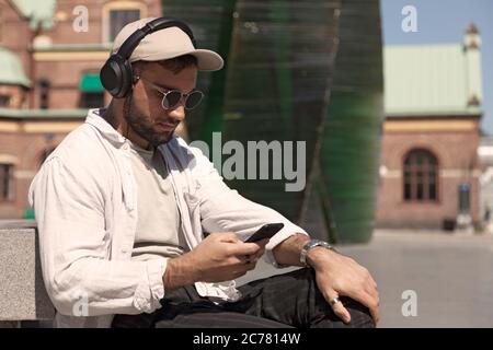 Umea, Norrland Schweden - 19. Juni 2020: Junger Mann sitzt und schaut auf sein Handy Stockfoto