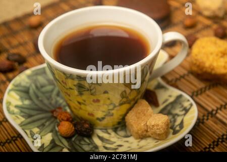 Eine Tasse Tee, getrocknete Hagebutte, Stücke von braunem Rohrzucker und Kekse auf einer Schilfmatte. Nahaufnahme Stockfoto