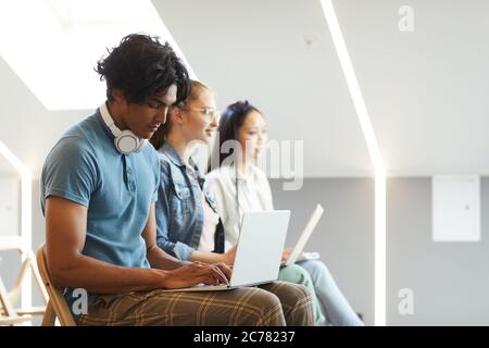 Seitenansicht konzentrierter multiethnischer Studenten, die in Reihe sitzen und Laptops für Notizen während des Vortrags verwenden Stockfoto