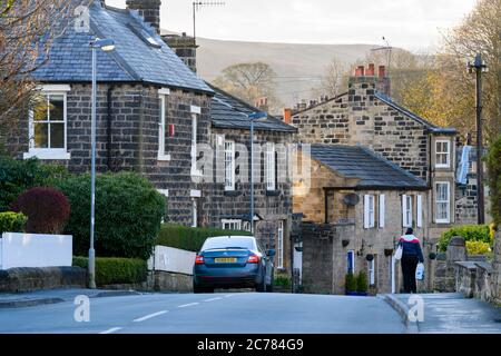 Hauptstraße in Menston Dorf (Frau, die an traditionellen Steinhäusern und Hütten vorbeiläuft) & landschaftlich reizvolle ländliche Moorlandschaft dahinter - West Yorkshire, England, Großbritannien. Stockfoto