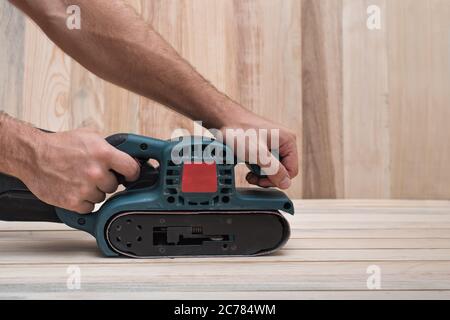 Elektrische Belt Sander, Schleifmaschine in männlicher Hand. Die Bearbeitung des Werkstücks auf hellbraunem Holz- Tabelle. Seitenansicht, in der Nähe Stockfoto