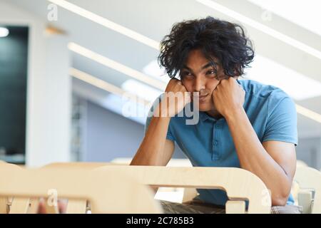 Erschöpft gemischt Rennen Kerl in blauem T-Shirt lehnte Kopf auf Fäusten während langweilige Vorlesung im Klassenzimmer hören Stockfoto
