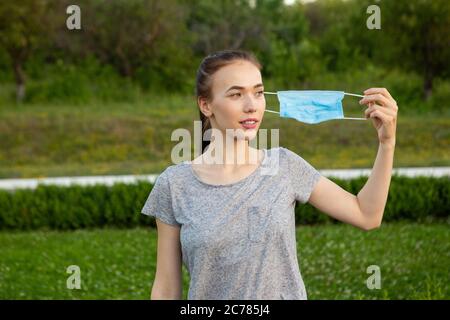 Junge Frau zieht die medizinische Maske aus und atmet tief und lächelnd zur Seite. Stockfoto