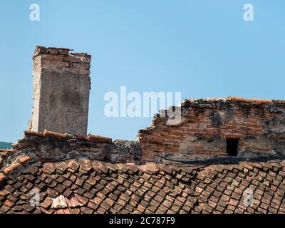 Altes mittelalterliches Dach mit roten Steinfliesen und einem abgenutzten Kamin, in Brasov Rumänien. Stockfoto