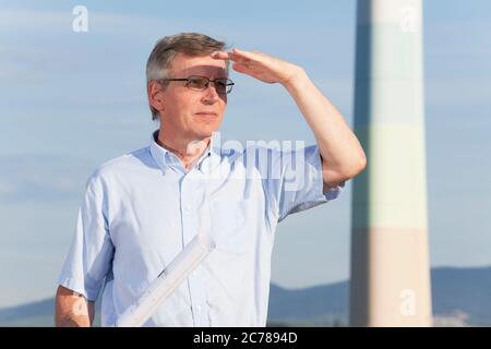 Architekt oder Ingenieur mit Blaupause in der Hand vor industriellem Hintergrund auf der Suche nach einer hellen Zukunft - selektiver Fokus auf die Person Stockfoto