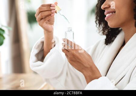 Schönheitsbehandlung Zu Hause. Lächelnde Afrikanische Frau Öffnungsflasche Mit Feuchtigkeitsspendenden Serum Stockfoto