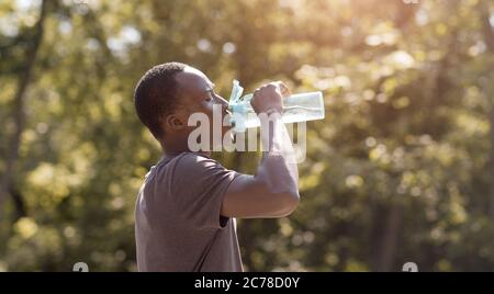 Überhitzter schwarzer Kerl, der Wasser aus der Flasche im Park trinkt Stockfoto