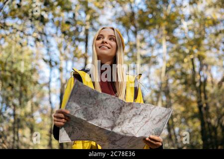 Schöne Hipster Frau mit Karte im Herbstwald navigieren. Fröhlicher Tourist, der versucht, den besten Weg zu finden. Aktiver Lebensstil, Reisekonzept Stockfoto