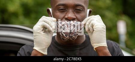 Hampshire, England, Großbritannien. 2020. Ein schwarzer Mann, der während des Covid-19-Ausbruchs eine Gesichtsmaske mit Tarnmuster und Schutzhandschuhe trägt, Stockfoto