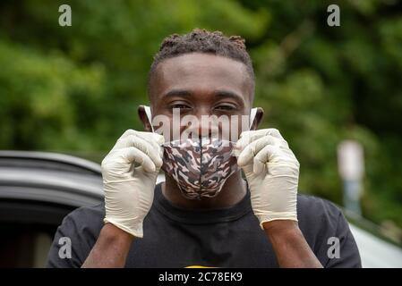 Hampshire, England, Großbritannien. 2020. Ein schwarzer Mann, der während des Covid-19-Ausbruchs eine Gesichtsmaske mit Tarnmuster und Schutzhandschuhe trägt, Stockfoto