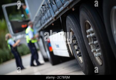 Unna, Deutschland. Juli 2020. Eine Polizistin und ein Polizist prüfen die Papiere eines LKW-Fahrers an einem Einsatzfahrzeug auf dem Kolberg-Parkplatz auf der Autobahn 2 in Richtung Hannover. Die Landpolizei Unna führt zusammen mit dem Landesamt für Bildung, Weiterbildung und Personalwesen (LAFP) und Zoll umfangreiche LKW-Kontrollen durch. Der Schwerpunkt der Kontrollen liegt auf der Einhaltung der Sozialvorschriften. Quelle: Jonas Güttler/dpa/Alamy Live News Stockfoto