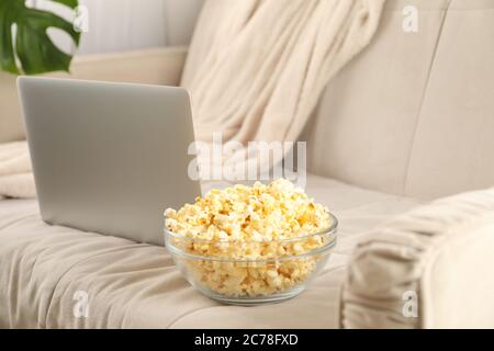 Eine Schüssel Popcorn und ein Laptop auf dem Sofa. Filme zu Hause ansehen Stockfoto