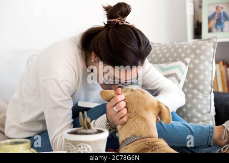 Junge Frau spielt und wird von ihrem Hund in ihrem Haus geküsst. Mädchen mit ihrem Haustier. Stockfoto