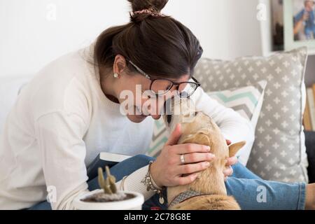 Junge Frau spielt und wird von ihrem Hund in ihrem Haus geküsst. Mädchen mit ihrem Haustier. Stockfoto