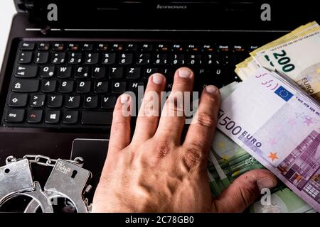 Bamberg, Deutschland. Juli 2020. Bamberg, Deutschland 13. Juli 2020: Symbolbilder - 2020 mehrere Tausend Euro in bar mit den Werten von 500 Euro, 200 Euro, 100 Euro und 50 Euro liegen auf einem Laptop mit Handschellen, Cyberkriminalität, Cyberkriminalität, Hand auf Tastatur, zur weltweiten Nutzung Quelle: dpa/Alamy Live News Stockfoto