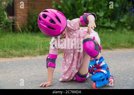 Ein kleines Mädchen Rollschuh in voller Schutz fiel auf den Asphalt. Das Konzept eines aktiven gesunden Lebensstils und sicheren Fahrens. Stockfoto