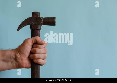 Die Hand des Schloßmeisters hält einen Vintage-Hammer mit einem Klauenhammer. Männliche Hand mit einem Hammer mit einem langen Holzgriff. Mann mittleren Alters der europäischen Rasse. Hand an Stockfoto