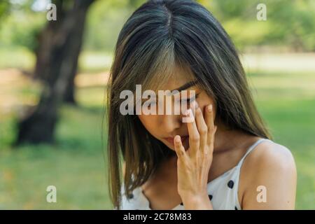 Junge Brünette Frau weinen und Tränen im Park wischen. Schönes Mädchen ist unglücklich und traurig im Freien. Stockfoto