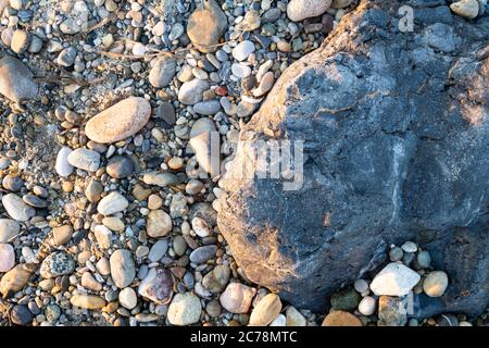 Ein großer grauer Stein und Kieselsteine am Strand für einen Hintergrund Stockfoto