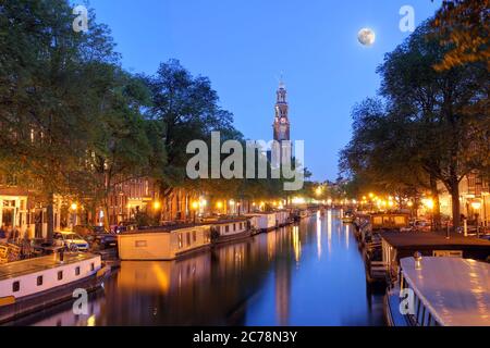 Nachtaufnahme des Prinsengracht-Kanals in Amsterdam (Niederlande) mit dem Turm von Westerkerk und Vollmond. Der überbelichtete Originalmond war repa Stockfoto