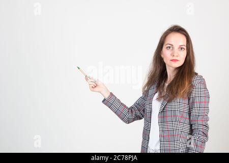 Schöne junge Frau in Business formelle Kleidung posiert gegen eine weiße Wand und zeigt auf etwas Stockfoto