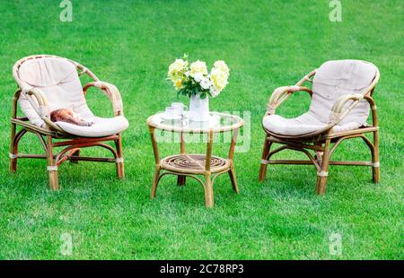 Zwei Sessel, Holzgartenmöbel auf Rasen im Freien zum Entspannen an heißen Sommertagen. Gartenlandschaft mit zwei Stühlen in der Natur, Blumen in Stockfoto