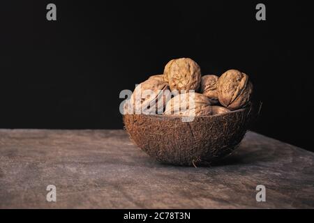 Gruppe von geschälten Walnüssen in einer Kokosnussschale Schale auf einem Holztisch auf schwarzem Hintergrund. Gesunde Ernährung. Stockfoto