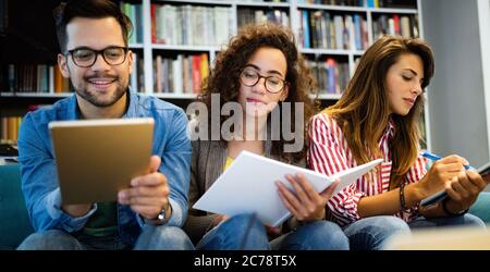 Gruppe glücklicher Studenten, die Bücher lesen und sich auf die Prüfung in der Bibliothek vorbereiten Stockfoto