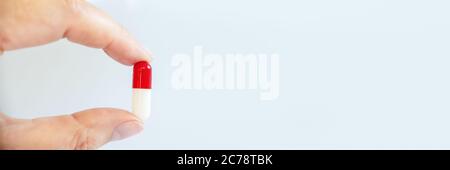 Nahaufnahme einer Hand mit einer weißen und roten Pille, Gesundheit und Medikamente Web-Banner Stockfoto