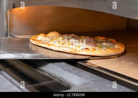 Die Pizza auf der Schaufel wird im Ofen gebraten. Der Prozess der Herstellung von italienischen Pizza in einem Restaurant. Stockfoto