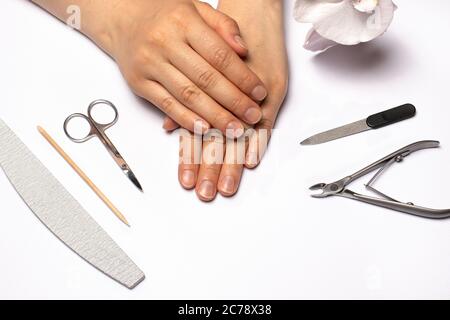 Weibliche Hände und Werkzeuge für die kantige Maniküre (Nagelfeile, Nagelhautzangen, Schere, Orangenstab). Nagelpflege zu Hause. Stockfoto