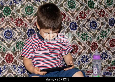 Ein kleiner Junge 2-3 Jahre alt schaut in den Bildschirm des Tablets. Cartoons für Kinder, Bildschirmzeit, Abhängigkeit der Kinder vom Computer und Telefon Stockfoto