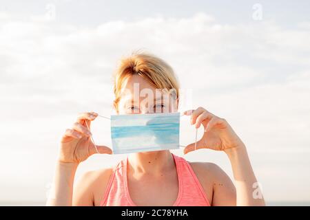 Portrait einer schönen blonden Frau mit einer Schutzmaske mit dem Himmel im Hintergrund, Konzept der Prävention und Gesundheitsversorgung, Copy Space für Text Stockfoto