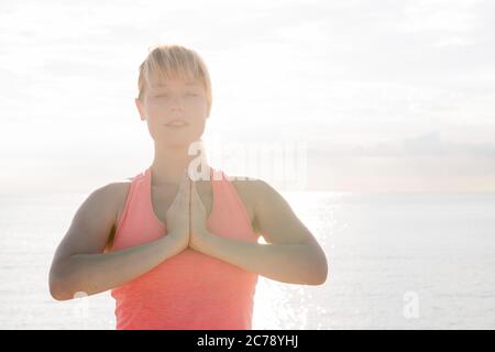 Portrait einer blonden Frau mit geschlossenen Augen Yoga bei Sonnenaufgang vor dem Meer praktizieren, Konzept der psychischen Gesundheitsversorgung und Entspannung, Kopierraum Stockfoto