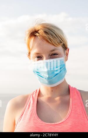 Vertikales Porträt einer schönen blonden Frau mit einer Schutzmaske mit dem Himmel im Hintergrund, Konzept der Prävention und Gesundheitsversorgung Stockfoto