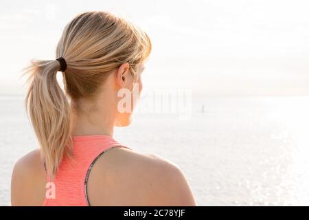 Rückansicht einer blonden Frau, die bei Sonnenaufgang Yoga praktiziert, vor dem Meer sitzend, Konzept für psychische Gesundheit und Entspannung, Textraum Stockfoto