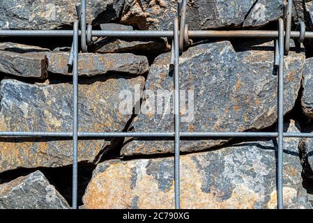 Hintergrund aus einer Steinwand mit einem verzinkten Metallgitter gesichert, Nahaufnahme. Stockfoto