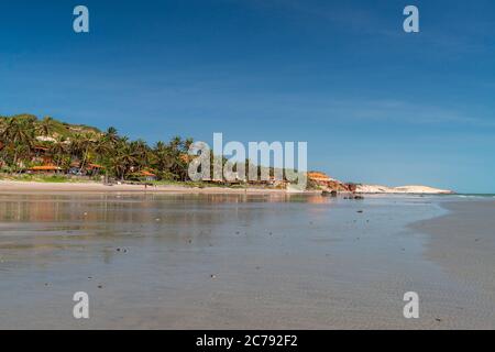 Farbige Steine und Sand am Strand, im Hintergrund Klippen mit natürlicher Vegetation in Praia de Peroba, Icapui, Ceara, Brasilien Stockfoto