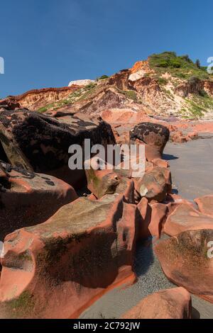 Farbige Steine und Sand am Strand, im Hintergrund Klippen mit natürlicher Vegetation in Praia de Peroba, Icapui, Ceara, Brasilien Stockfoto