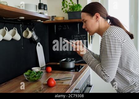 Frau, die in der Küche telefoniert Fotos von ihrem Essen machte Stockfoto
