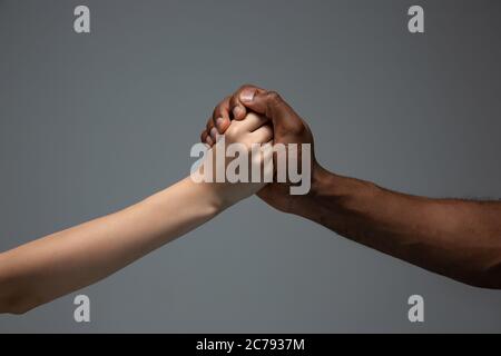 Unterstützen, Helfen. Rassistische Toleranz. Respektieren Sie die soziale Einheit. Afrikanische und kaukasische Hände gestikulieren auf grauem Studiohintergrund. Menschenrechte, Freundschaft, Konzept der Einheit der Intenationalen. Interrassische Einheit. Stockfoto