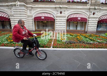 Moskau, Russland. Juli 2020. Ein Mann fährt am 15. Juli 2020 bei einem jährlichen Blumenfest vor dem KAUGUMMI-Kaufhaus in der Nähe des Roten Platzes im Zentrum von Moskau, Russland, an Blumen vorbei. In diesem Jahr wurden rund 200,000 Blumen in und außerhalb des KAUFHAUSES FÜR KAUGUMMI gepflanzt. Quelle: Alexander Zemlianichenko Jr/Xinhua/Alamy Live News Stockfoto