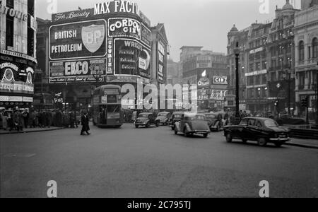 Vintage-Fotografie des Piccadilly Circus aus den 1950er Jahren in London, England. Zeigt die Neon-Werbezeichen der Ära. Zeigt auch den Verkehr in der Gegend, Autos und Lieferwagen. Stockfoto