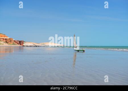 Kleines Fischerboot, das bei Ebbe, am frühen Morgen, im Hintergrund Dünen und Klippen am Strand von Peroba, Icapui, Ceará, Brasilien verankert Stockfoto