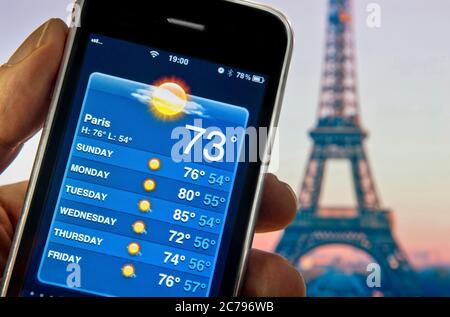 PARIS Weather Forecast Smartphone App Application 4G/5G Eiffelturm in der Abenddämmerung mit der Hand hält Apple iPhone Smartphone mit Bildschirm zeigt 73F Grad und Woche der Urlaubssonne auf dem Bildschirm Wetter Smartphone-Anwendung Paris Frankreich Stockfoto