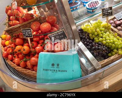 Fortnum & Mason Food Hall mit polierten perfekt gewaschenen Tomaten und Trauben zum Verkauf mit eleganten Fortnum's Marken recyclingfähigen Papiertaschen, platziert für den bequemen Einkauf. Pflaumentomaten und Rindertomaten im Weidenkorb. Fortnum & Mason Food Hall Department, Piccadilly St. James's, London W1A 1ER Stockfoto